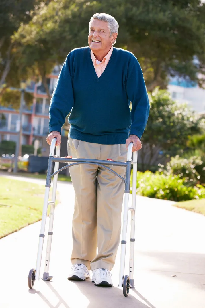 An older man walking with a frame in a park, smiling